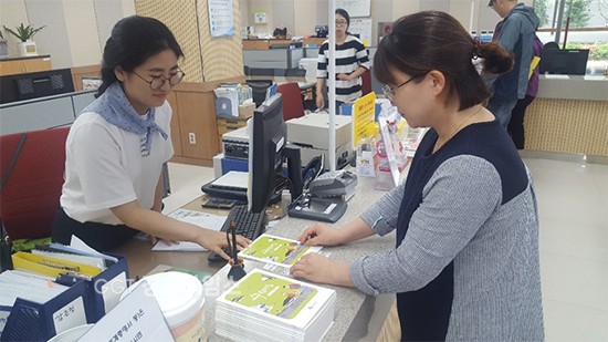 주민센터 직원이 전입시민에게 '수원마을'을 건네주고 있다.ⓒ경기타임스
