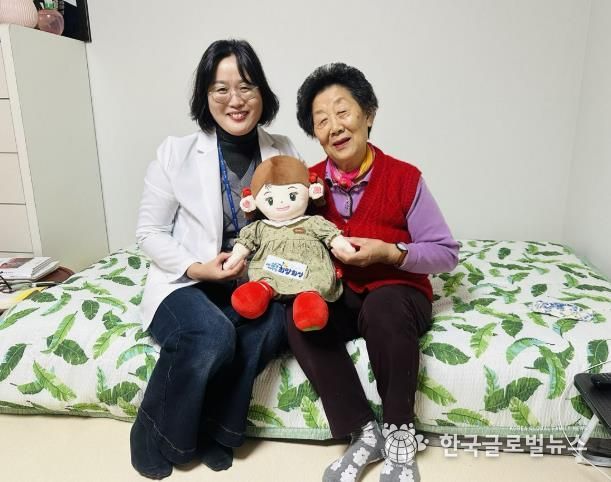 화성시동탄보건소 관계자와 독거 어르신이 AI 돌봄로봇 ‘효돌이’를 함께 들고 환하게 웃고 있다